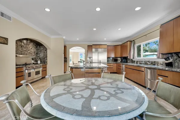a room with stainless steel appliances kitchen island granite countertop a stove a sink a dining table and chairs