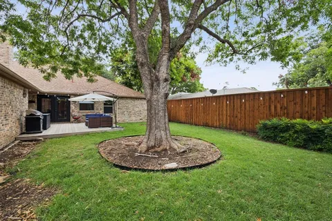a view of a backyard with table and chairs potted plants and large tree