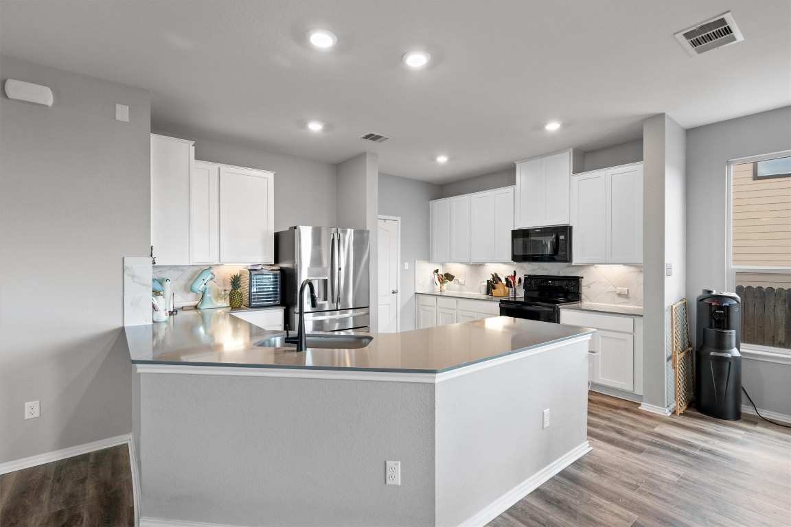 323 Gustaf Trail Kyle, TX 78640 - Photo 1 of 1 a kitchen with kitchen island granite countertop a stove top oven a sink dishwasher a refrigerator and white cabinets with wooden floor