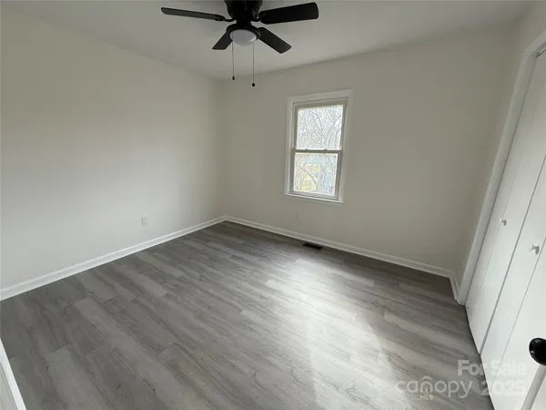 an empty room with wooden floor fan and windows