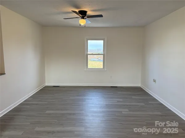 an empty room with wooden floor chandelier fan and windows