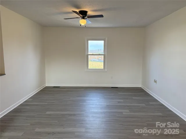 an empty room with wooden floor chandelier fan and windows