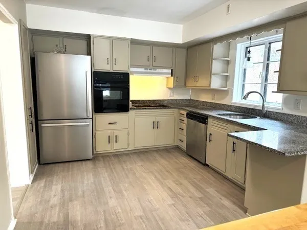 a kitchen with granite countertop a refrigerator a sink and white cabinets