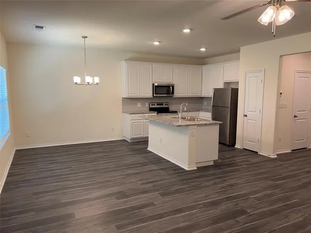 a kitchen with stainless steel appliances granite countertop a stove top oven a refrigerator a sink and a wooden floor