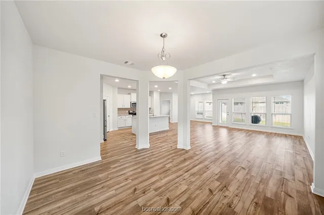 a view of an empty room with wooden floor and a kitchen
