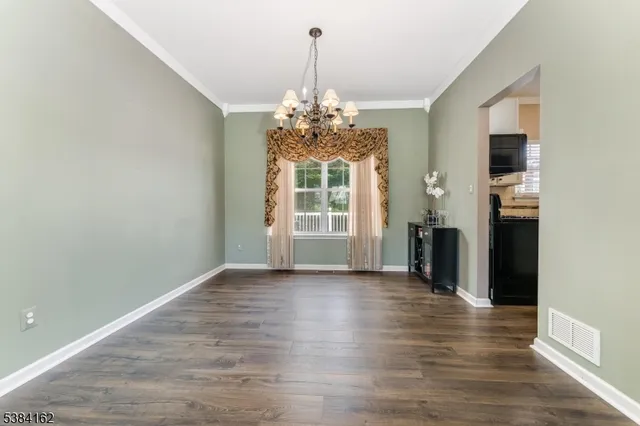 an empty room with wooden floor chandelier and windows