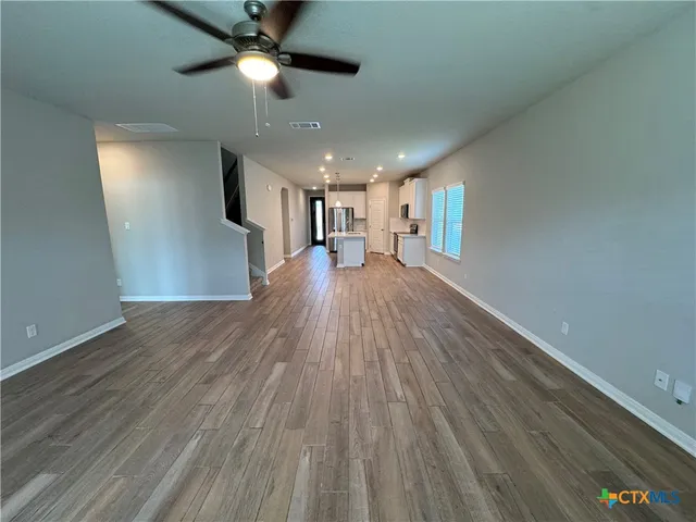 a view of a room with wooden floor a ceiling fan and windows