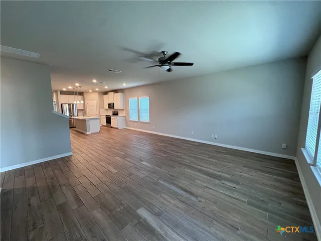 an empty room with wooden floor chandelier fan and windows