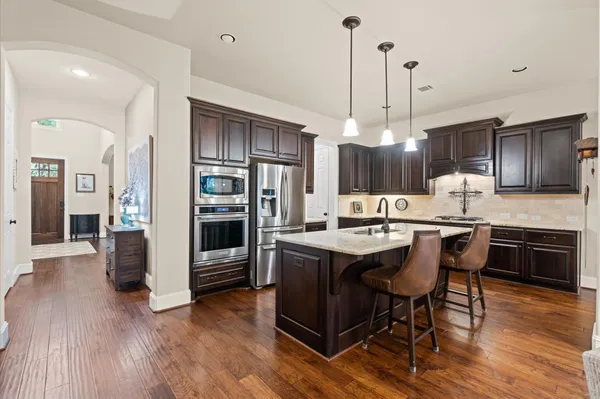 a kitchen with stainless steel appliances granite countertop a sink a stove a refrigerator and island with wooden floor