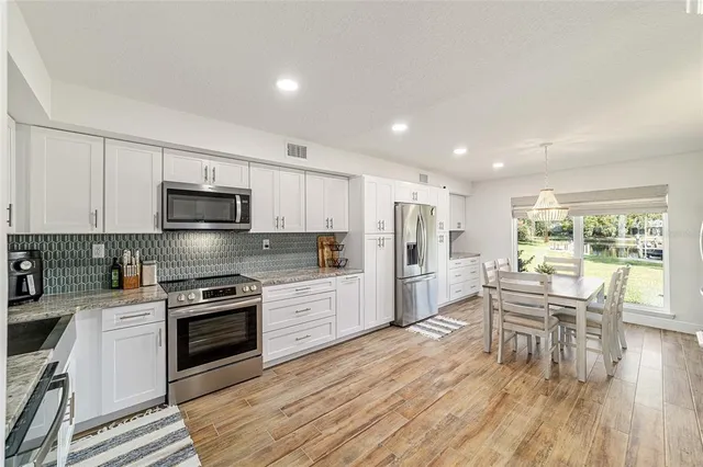 a kitchen with stainless steel appliances a stove a sink dishwasher a refrigerator with white cabinets and wooden floor