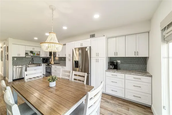a kitchen with stainless steel appliances kitchen island granite countertop a refrigerator a stove a sink dishwasher and white cabinets with wooden floor