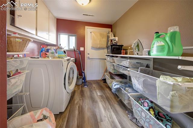 2415 Sturgis Road Colorado Springs, CO 80909 - Photo 10 of 10 Laundry room featuring washing machine and clothes dryer, visible vents, wood finished floors, cabinet space, and wainscoting