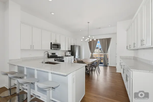 a kitchen with stainless steel appliances granite countertop a stove top oven a sink a dining table and chairs with wooden floor