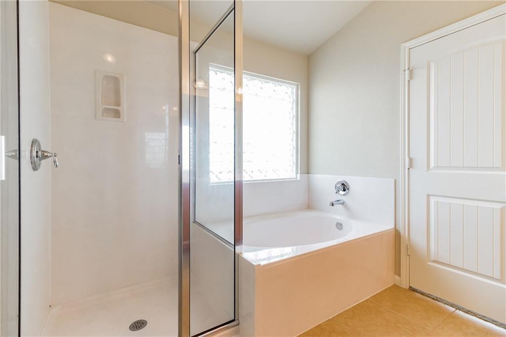 8505 Inca Dove Drive Austin, TX 78729 - Photo 20 of 30 The bathroom features a walk-in shower with a glass enclosure, a built-in bathtub with a chrome faucet, and a window with textured glass