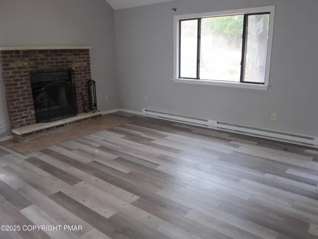 an empty room with wooden floor fireplace and windows