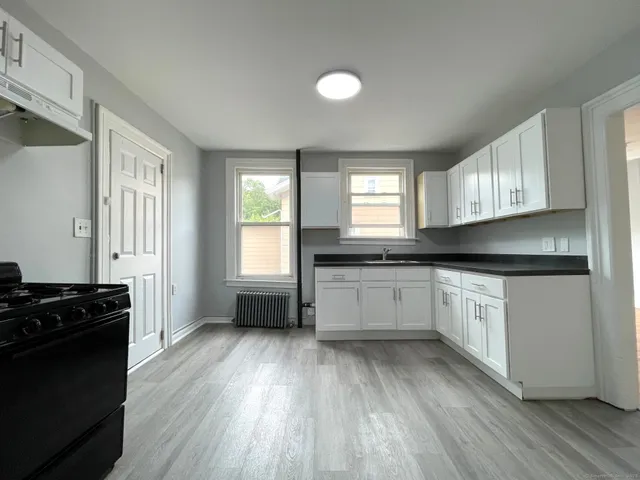 a kitchen with granite countertop a stove a sink wooden floor cabinets and a window