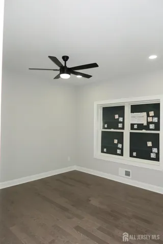 a view of an empty room with wooden floor and a ceiling fan