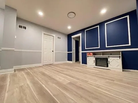 a view of an empty room with wooden floor and kitchen
