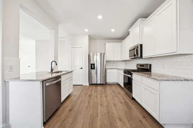 a kitchen with granite countertop a sink stove refrigerator and white cabinets with wooden floor