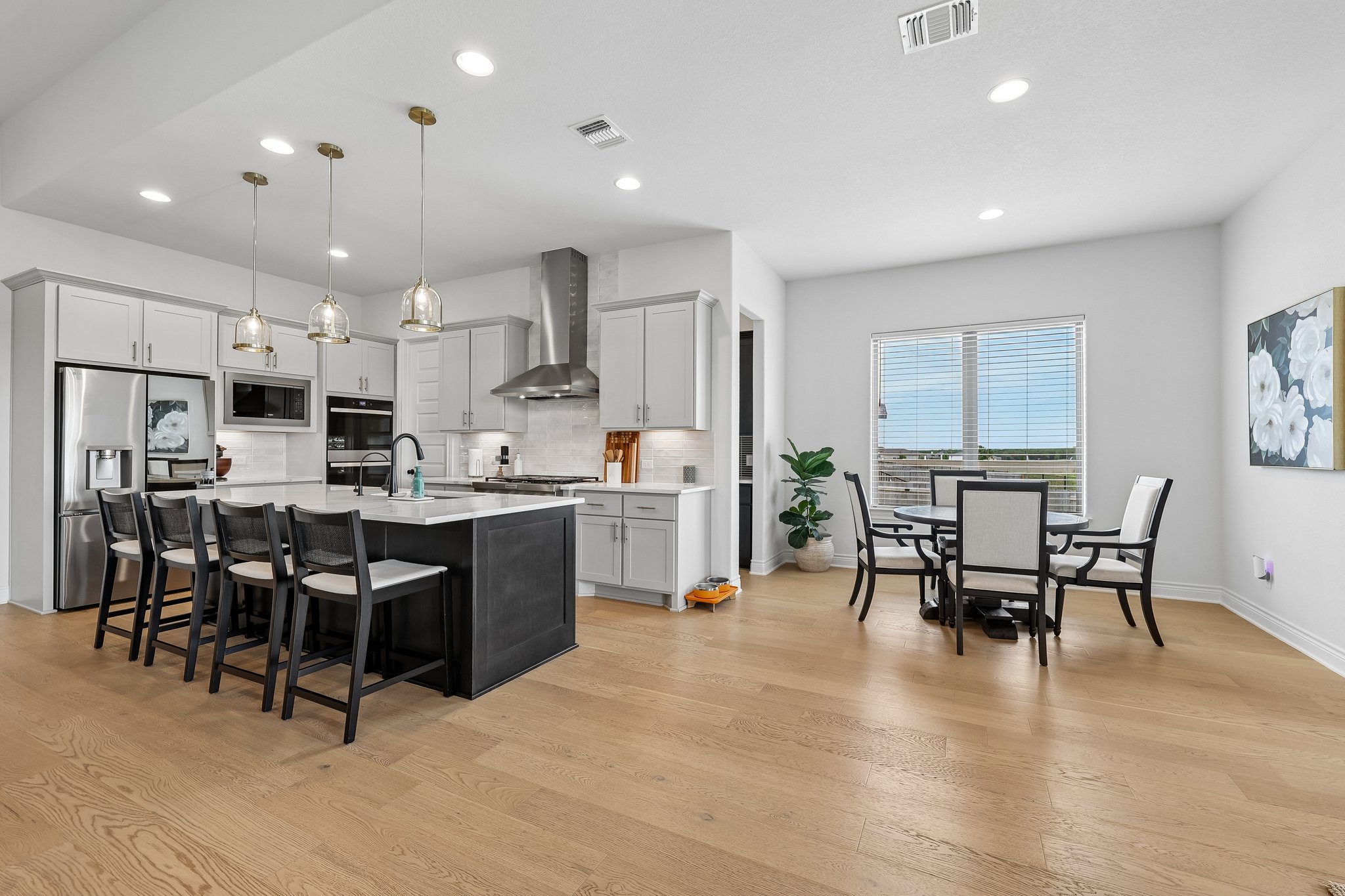 130 Firethorn Loop Bastrop, TX 78602 - Photo 11 of 38 Modern kitchen featuring light gray cabinetry, stainless steel appliances, a dark-toned island with seating, pendant lighting, and wood-finish flooring