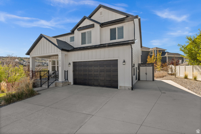 14728 South Canyon Pointe Road Draper, UT 84020 - Photo 3 of 35 Contemporary two-story residence featuring white board and batten siding, dark-framed windows with louvered shutters, a covered porch with black railings, a two-car garage with a dark panel door, and an extended concrete driveway