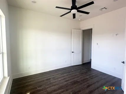 an empty room with wooden floor a ceiling fan and windows