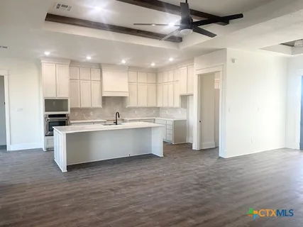 a large white kitchen with kitchen island a sink wooden floor and a refrigerator