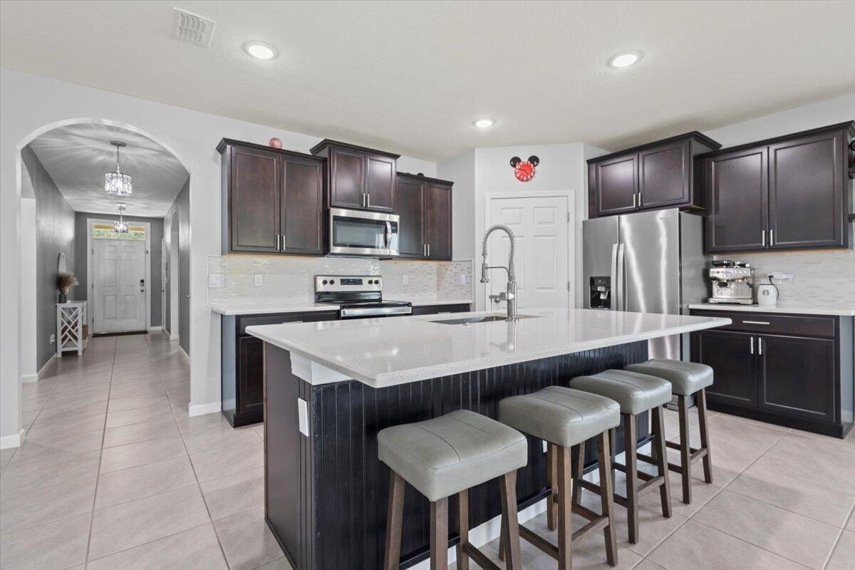 a kitchen with kitchen island granite countertop a sink a stove a refrigerator cabinets and chairs