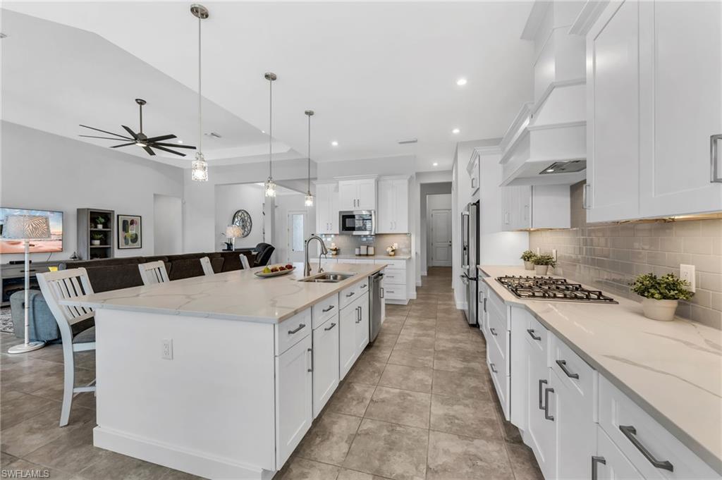 3410 Wellfleet Lane Naples, FL 34114 - Photo 9 of 28 a large white kitchen with kitchen island a stove a sink a refrigerator and a dining table with wooden floor