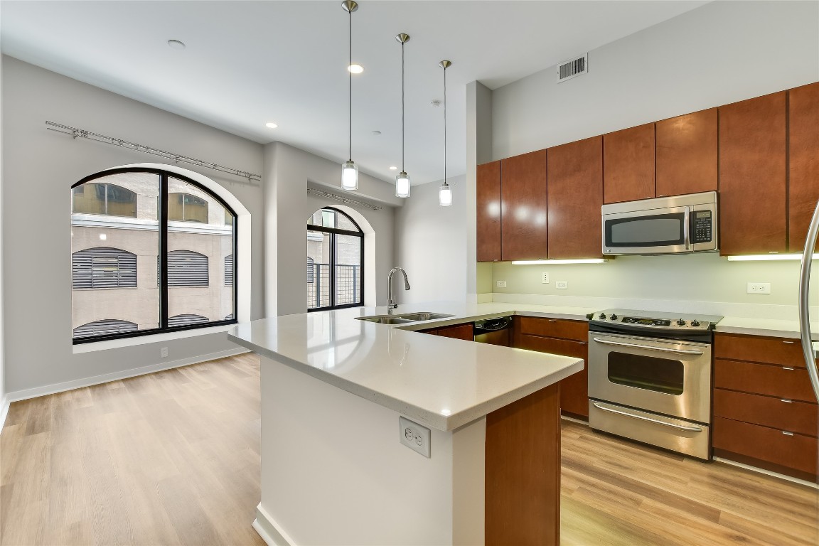 507 Sabine Street, Unit 709 Austin, TX 78701 - Photo 7 of 13 Kitchen with stainless steel appliances, light wood-type flooring, a peninsula, pendant lighting, and recessed lighting