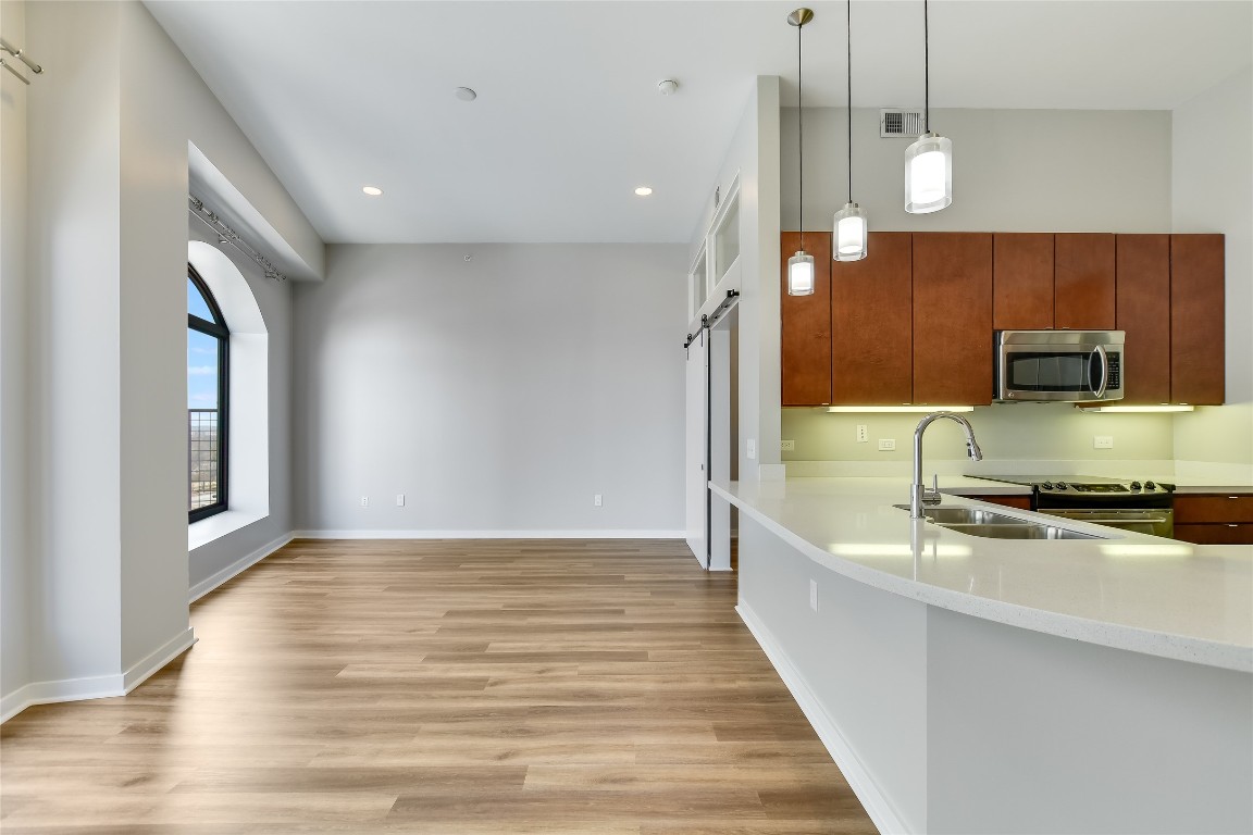 507 Sabine Street, Unit 709 Austin, TX 78701 - Photo 8 of 13 Kitchen with stainless steel microwave, a barn door, light wood-style flooring, light stone counters, and pendant lighting