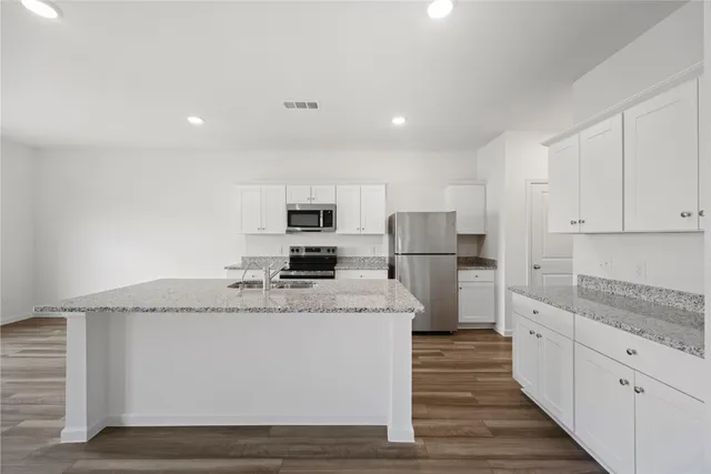 a kitchen with granite countertop stainless steel appliances a sink stove refrigerator and white cabinets with wooden floor