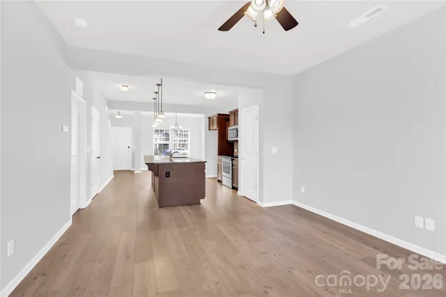 an empty room with kitchen view and a ceiling fan