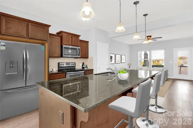 a kitchen with stainless steel appliances granite countertop a refrigerator a stove a sink a dining table and chairs with wooden floor