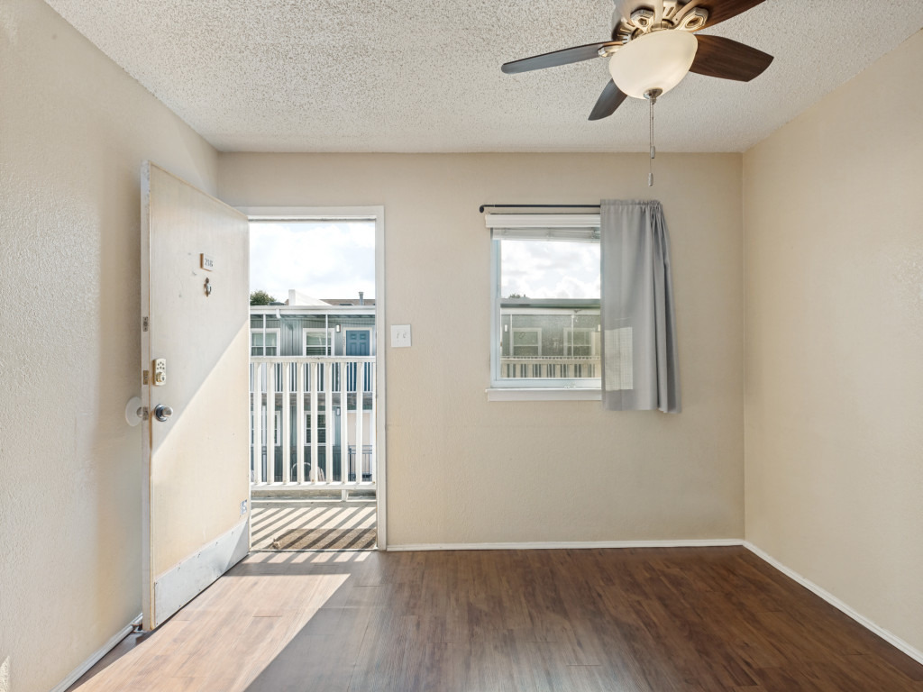 2401 Manor Road, Unit 218 Austin, TX 78722 - Photo 14 of 27 Rich wood flooring extends through this room, illuminated by a large window and a ceiling fan providing gentle air circulation.
