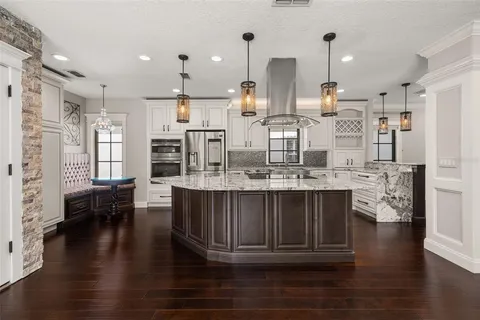 a kitchen with stainless steel appliances kitchen island granite countertop a refrigerator a stove a oven and white cabinets with wooden floor