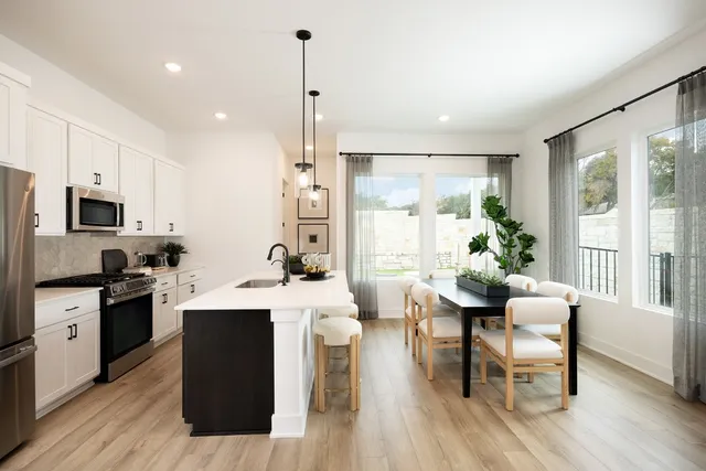 a room with stainless steel appliances kitchen island granite countertop a dining table chairs and a wooden floor