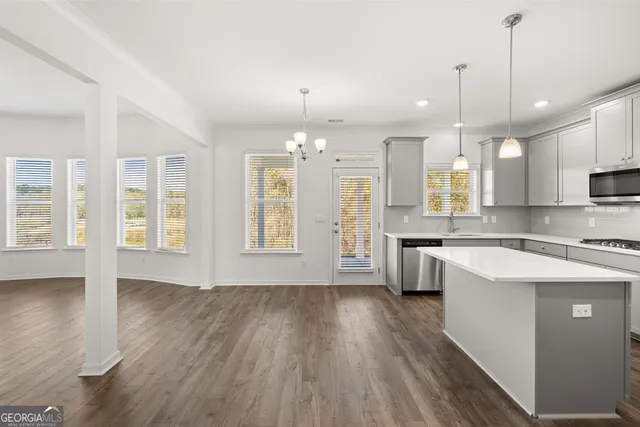 a view of an empty room with wooden floor and a kitchen