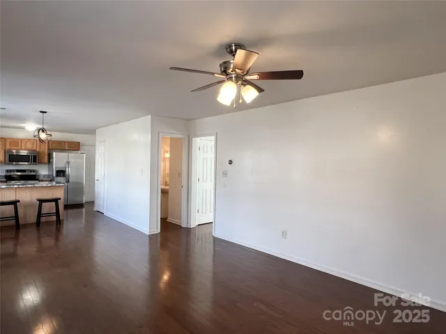 a view of an empty room and kitchen with wooden floor
