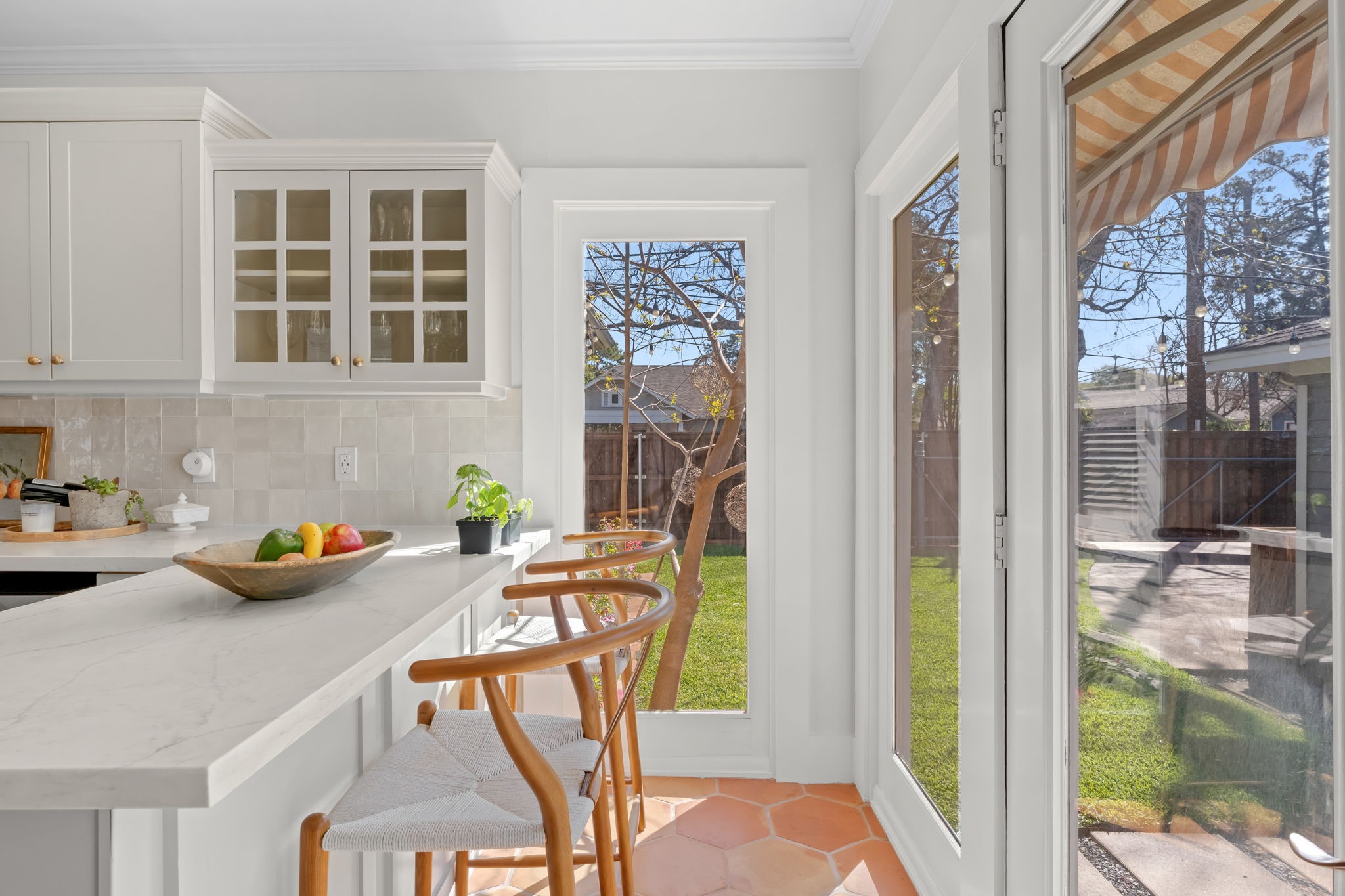 1002 West Cottage Street Houston, TX 77009 - Photo 12 of 37 The island provides casual seating and additional prep space, positioned right next to floor-to-ceiling windows and French doors that look out to the fenced backyard. Natural light fills this end of the kitchen throughout the day, with mature trees visible just beyond the awning. It's a layout that connects indoor and outdoor living without any effort.