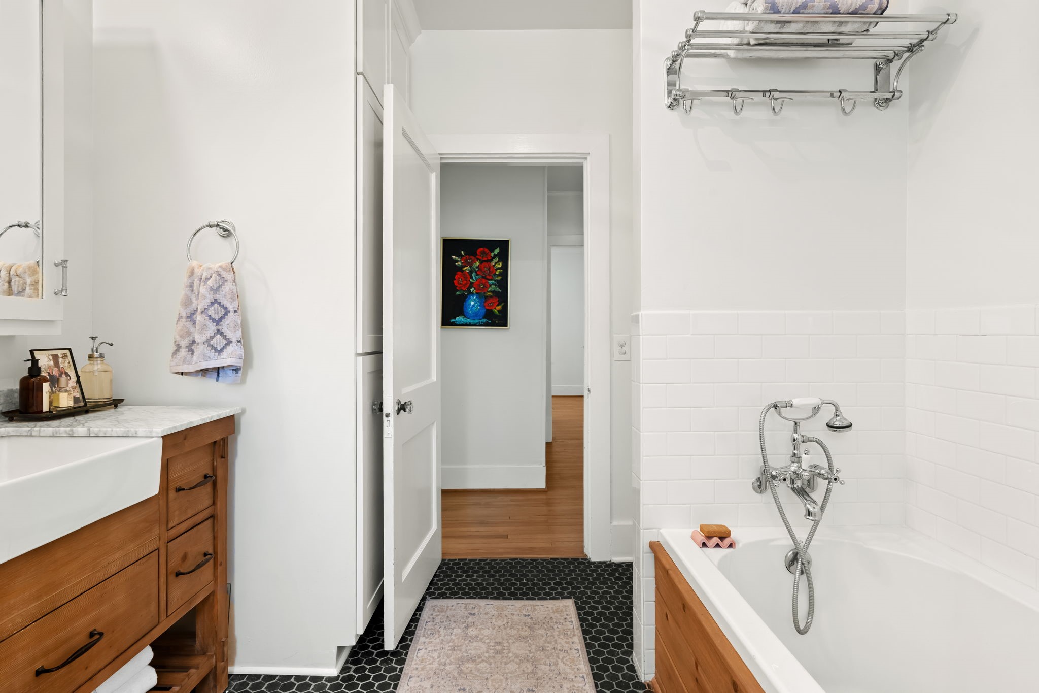 1002 West Cottage Street Houston, TX 77009 - Photo 14 of 37 The full bath features a soaking tub with classic subway tile surround, hex tile flooring, and polished chrome fixtures. A wood vanity with marble countertop and farmhouse-style basin sits opposite the tub, with the doorway opening to the hallway and bedrooms. This bathroom serves the first-floor bedrooms and is centrally located within the home's layout.