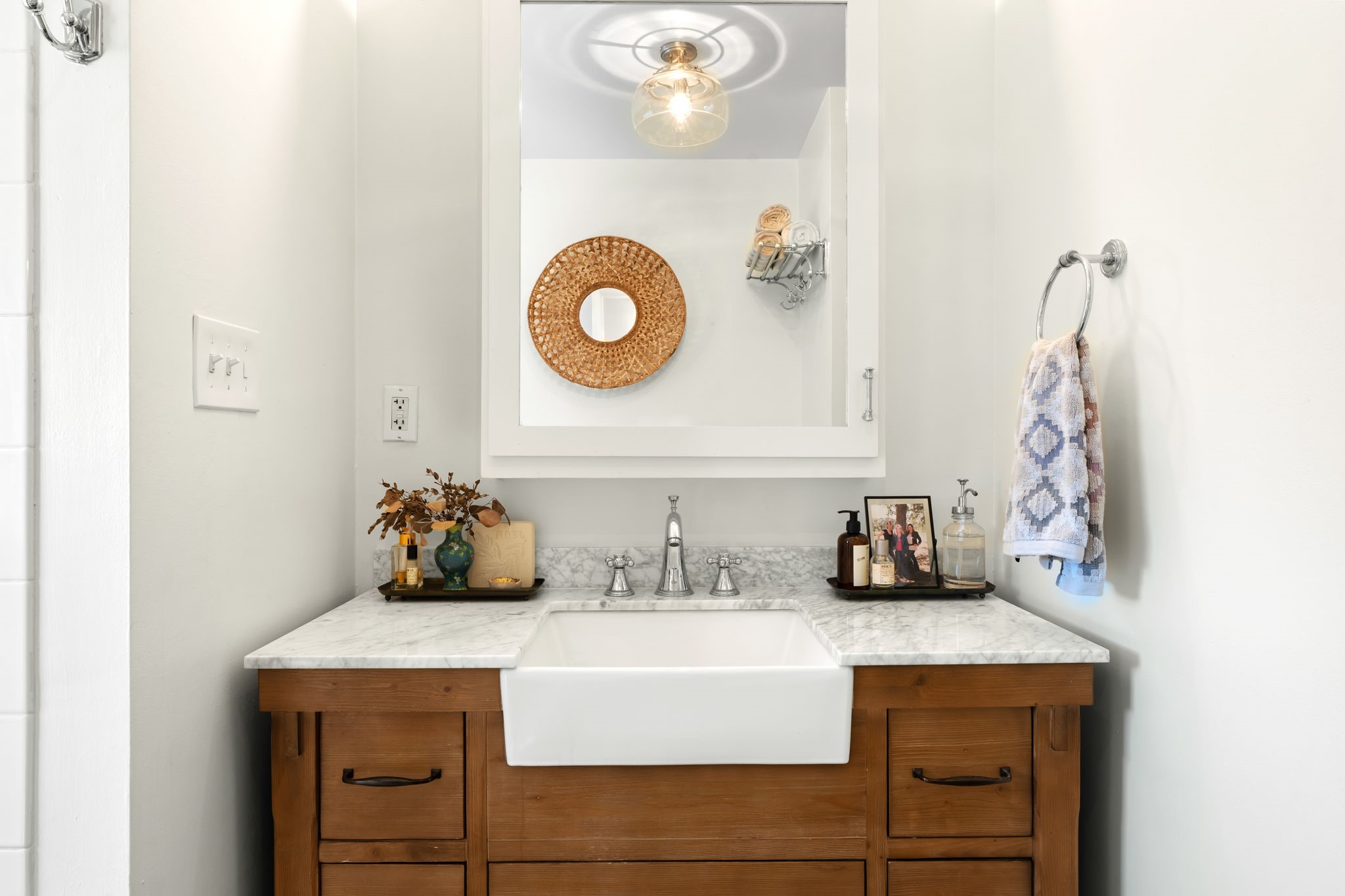 1002 West Cottage Street Houston, TX 77009 - Photo 15 of 37 A closer look at the vanity shows the farmhouse-style basin, marble countertop, and warm wood cabinetry with ample drawer storage below. Chrome hardware and a glass pendant light fixture keep the look clean and cohesive with the rest of the home. There's solid counter space on both sides of the sink for everyday use.
