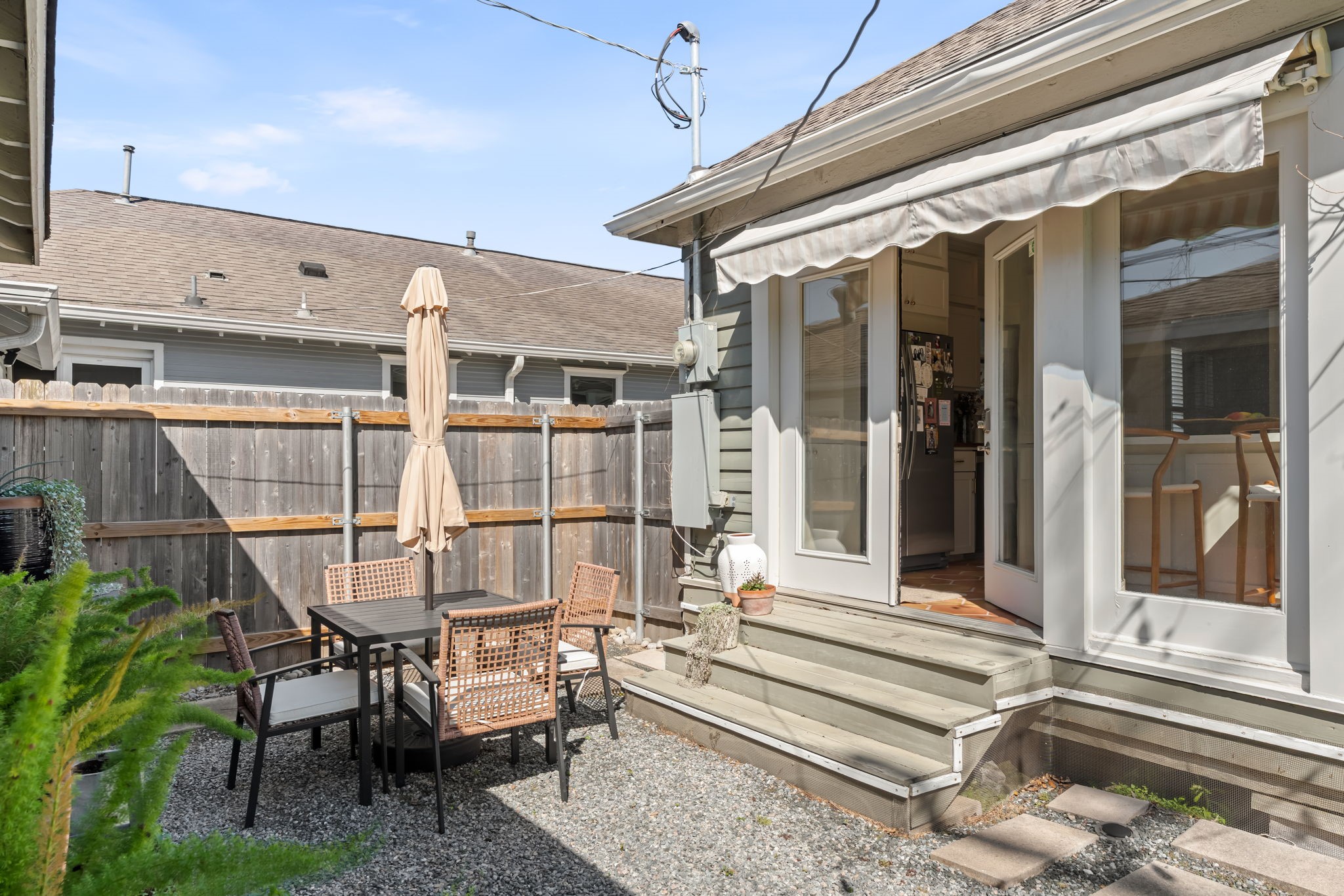 1002 West Cottage Street Houston, TX 77009 - Photo 24 of 37 Step out through the kitchen's French doors onto a raised deck with an awning a natural spot for morning coffee or outdoor dining. The fenced backyard beyond offers privacy, and the gravel patio area provides additional usable space right off the steps. This kind of indoor-outdoor connection from the kitchen is a daily-use feature, not just a weekend perk.