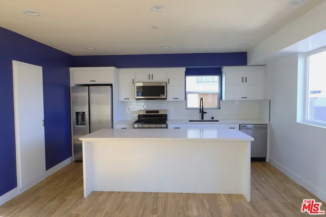 a view of a kitchen with stainless steel appliances a sink dishwasher a refrigerator and wooden floor
