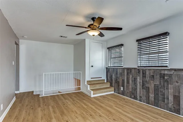 a view of an empty room with wooden floor and a ceiling fan