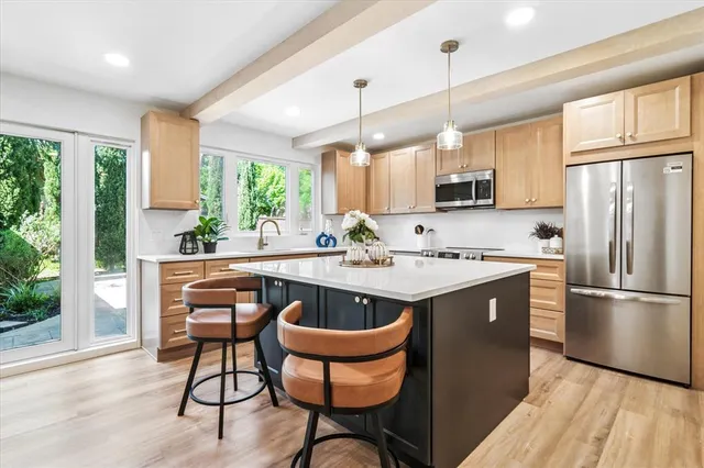 a kitchen with stainless steel appliances granite countertop a sink a stove a refrigerator cabinets and a dining table with wooden floor