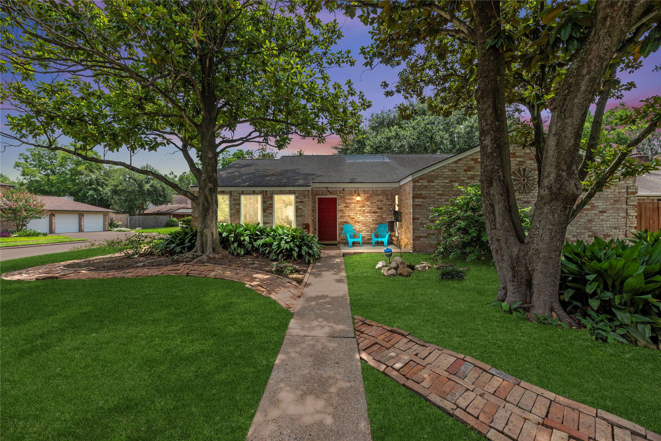 14203 Wickersham Lane Houston, TX 77077 - Photo 1 of 25 Captivating twilight view of the single-story brick home, showcasing a welcoming red front door, mature shade trees, and a beautifully manicured lawn accented by custom brick border walkways.