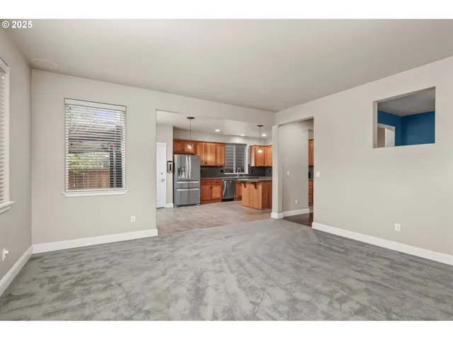 a view of an empty room with kitchen and window