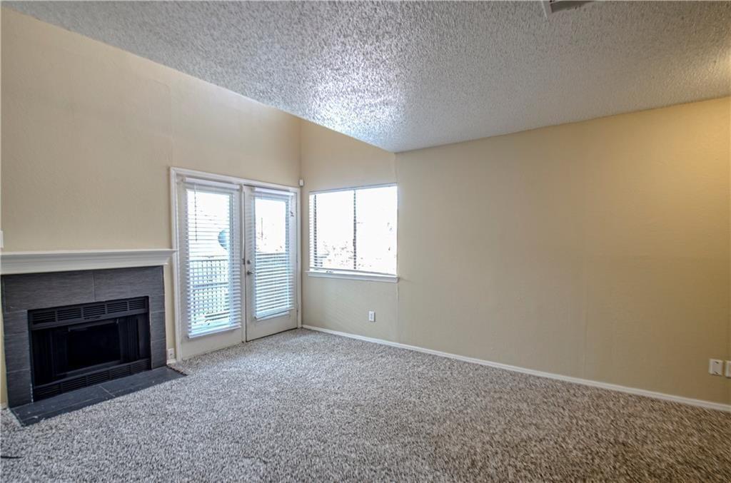 9835 Walnut Street, Unit 202 Dallas, TX 75243 - Photo 11 of 19 Living area featuring a textured ceiling, a fireplace with a dark tile surround and white mantel, light-colored walls, and gray carpet flooring