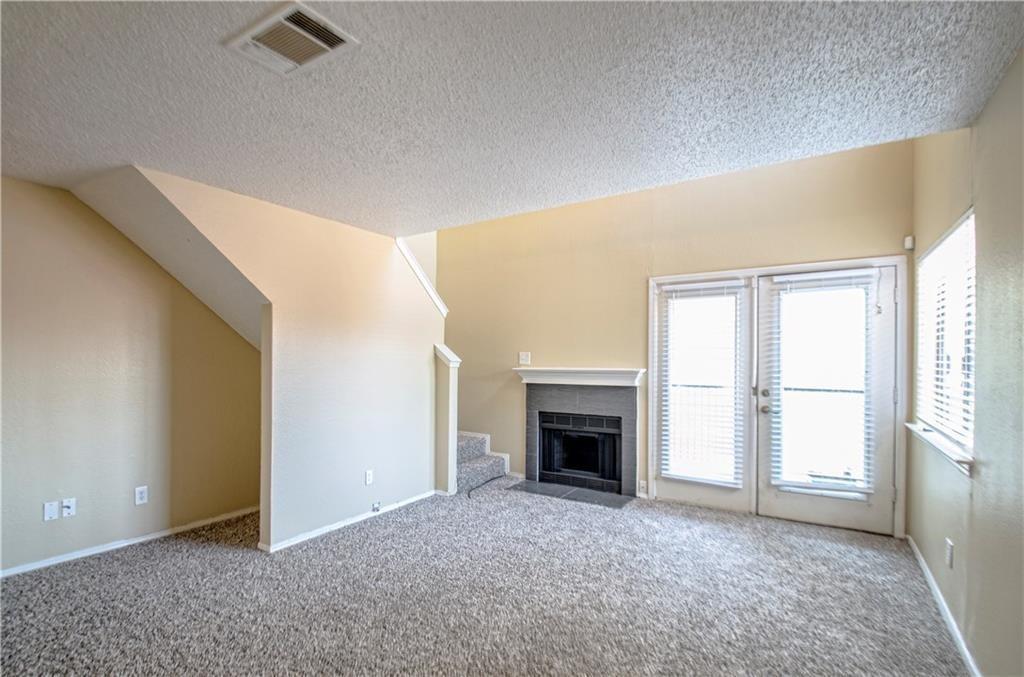 9835 Walnut Street, Unit 202 Dallas, TX 75243 - Photo 12 of 19 Living area featuring a fireplace with a grey tile surround and white mantel, light-colored carpeting, and a staircase with matching carpeted treads